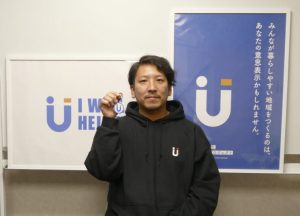 田中さんがI will help youのキーホルダーをもってポーズしている